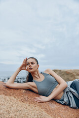 A young woman of Eastern European descent in activewear, lying on a rock with a calm expression,...