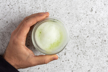 Barista holding a glass of matcha latte with milk foam on marble countertop