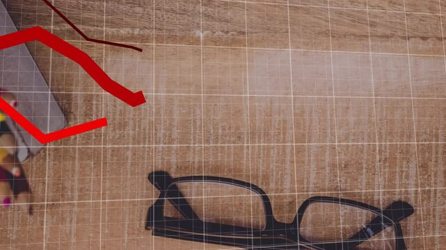 Black eyeglasses sitting on wooden desk, showing pencils, notebook with red trendline grid overlay