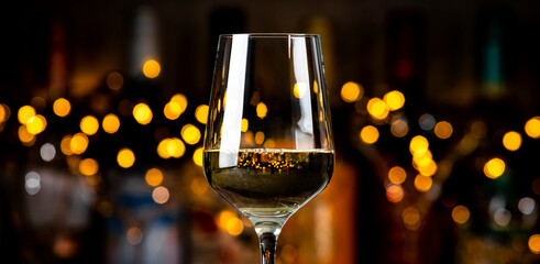 White Chardonnay wine glass and wine bottles on dark bar background with lights