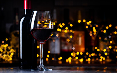 Dry red wine Cabernet Sauvignon in glass and wine bottle on dark bar background with lights