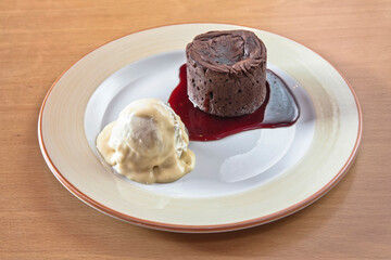 Chocolate fondant with strawberry sauce and a scoop of ice cream on a wooden table, desserts