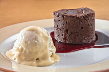 Chocolate fondant with strawberry sauce and a scoop of ice cream on a wooden table, desserts