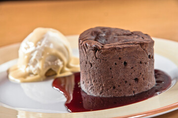 Chocolate fondant with strawberry sauce and a scoop of ice cream on a wooden table, desserts