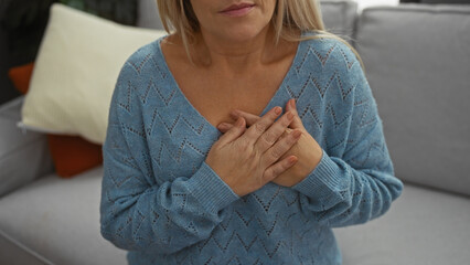 Woman in blue sweater clasping hands on chest in cozy living room, expressing emotion, surrounded...