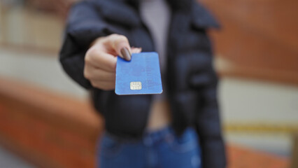Woman holding credit card in urban street with blurred background, showcasing payment technology in an outdoor city setting.