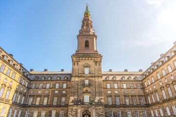 Obraz premium Visitors admire the stunning architecture of Christiansborg Palace in Copenhagen, surrounded by historical charm under a bright blue sky. The grandeur of this government building captivates all.