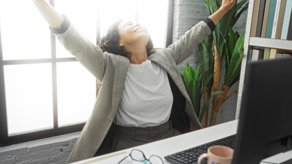 Woman rejoicing in modern office interior with arms raised near window showcasing vibrant work environment and personal achievement.