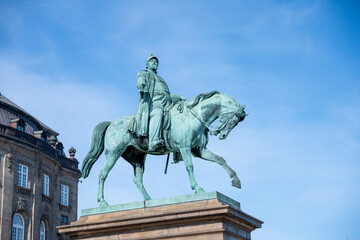 Fototapeta premium This striking statue of Frederick VII, a significant Danish monarch, stands tall on horseback in Copenhagen, surrounded by historical buildings against a clear blue sky.