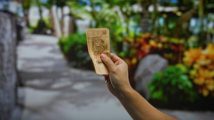 Man holding brazilian reais banknotes in an outdoor urban park setting, highlighting money and...