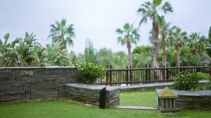 Blurred view of a luxurious tropical resort garden featuring lush greenery with palm trees, stone walls, and a serene atmosphere in an outdoor hotel setting.