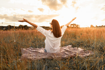 Young woman sitting in field under sunset light
