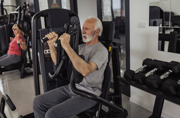 Two determined pensioners in gym doing chest exercises