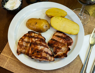 Grilled pork pieces with boiled half potatoes served in a plate with necessary table laying