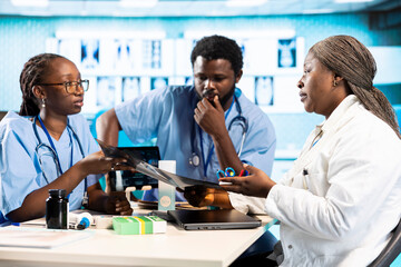 Black expert discussing with junior nurses to find the best treatment options, showcasing teamwork...