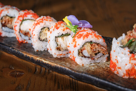 Soft shell crab uramaki sushi rolls with masago and edible flower garnish on serving plate
