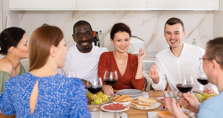 Happy adult friends at the festive table discussing the news and drinking red wine