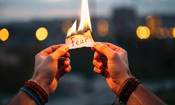 Two hands hold burning paper with word "Fear," symbolizing overcoming fear