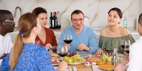 Multicultural female and male friends chatting and drinking wine at table