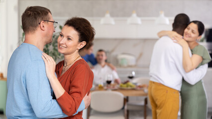 Positive woman in terracotta dress tenderly embracing man, enjoying slow dance at cozy friendly house party..