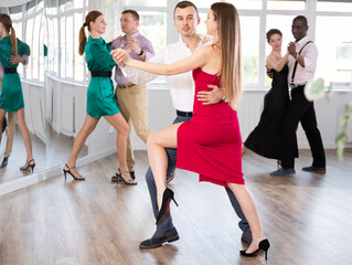 Fototapeta premium Positive young man and woman practicing waltz in pair in dancing studio