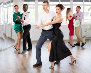 Fototapeta premium Dynamic young male and female attendees of dancing courses doing waltz in group
