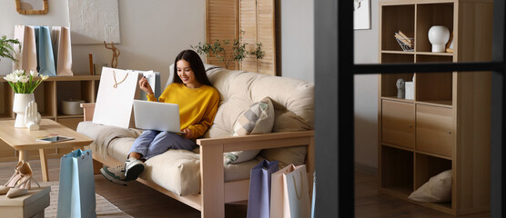 Young Asian woman with laptop and credit card shopping online at home