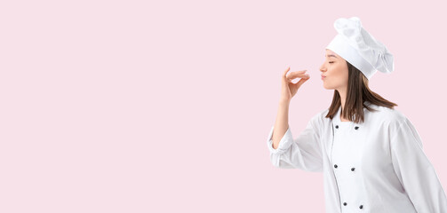 Young female chef in uniform making delicious gesture on pink background