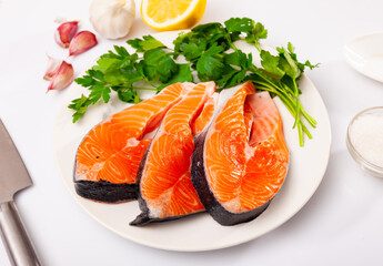 Raw salmon steaks on plate with garlic, lemon and parsley. Isolated over white background.