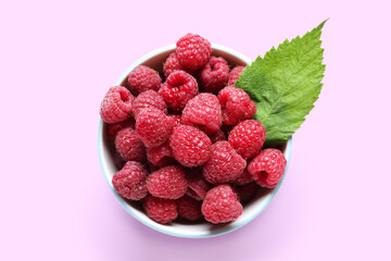 Bowl with fresh ripe raspberries and leaf on lilac background