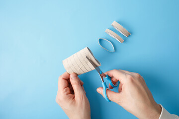 a simple craft project in progress. Two hands are shown, using blue-handled scissors to cut a...