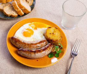 Two delicious fried sausages with fried eggs, sliced potatoes and decorated with a fresh sprig of parsley
