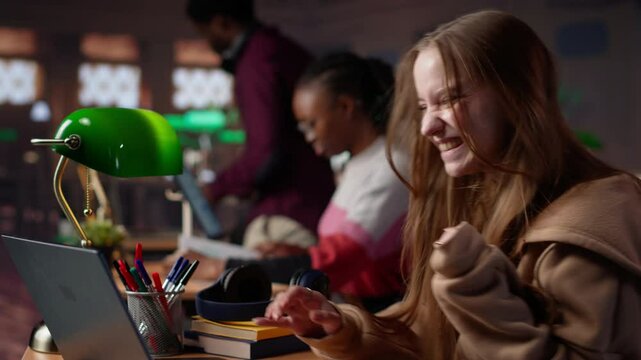Girl shares a high five with her african american colleague at the library, receiving high grades on a group assignment at school. Pleased clever pupils celebrating academic success. Camera A.