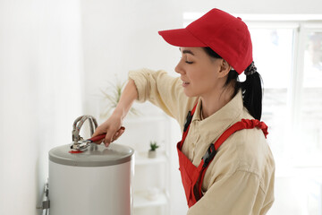 Female worker with wrench installing modern electric boiler in bathroom
