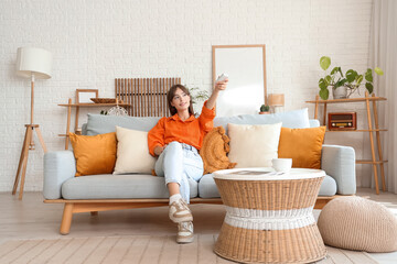 Pretty young woman with air conditioner remote control sitting on sofa