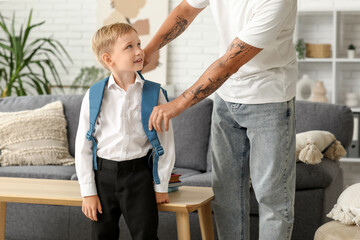 Father adjusting his little son's backpack at home