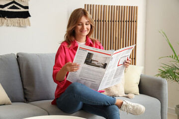 Pretty young woman with newspaper sitting on cozy sofa at home