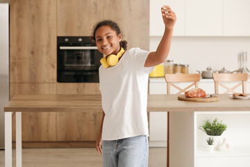 Happy African-American girl with headphones dancing at home