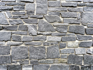 Close-up of natural gray stone wall texture with rough uneven surface, detailed masonry pattern background for architecture, design, and construction projects