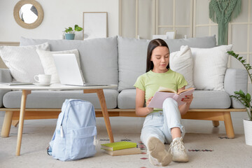 Fototapeta premium Female student reading book on floor at home