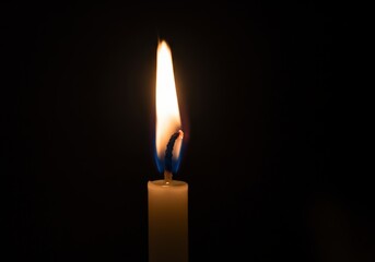 A single candle flame glows brightly against a black background, offering a warm and inviting light.