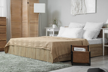 Interior of stylish bedroom with comfy bed, magazines and wooden furniture