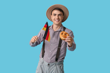 Young man in traditional German clothes holding flag and pretzel on blue background. Octoberfest concept