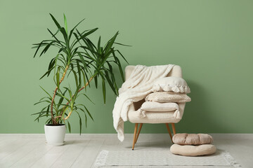 White armchair with cushions and houseplant near green wall