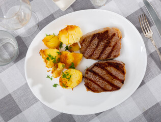 Portion of just cooked grilled beef steak with roasted potatoes.