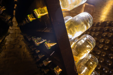 Obraz premium Bottles on racks in deep and long undergrounds caves, making champagne sparkling wine from chardonnay and pinor noir grapes in Reims, Champagne, France