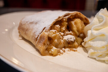 Austrian desserts, piece of apple strudel with whipped cream served in old traditional bakery cafe in Vienna, close up