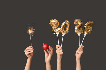 Female hands with figure 2025 made of foil balloons, sparkler and Christmas ball on black background