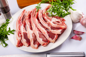 Raw hogget chops on ribs on plate with fresh fragrant arugula leaves, garlic and seasonings. Main ingredients for cooking ..