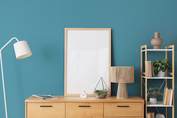 Modern chest of drawers with floor lamp, shelving unit and frame near blue wall in room